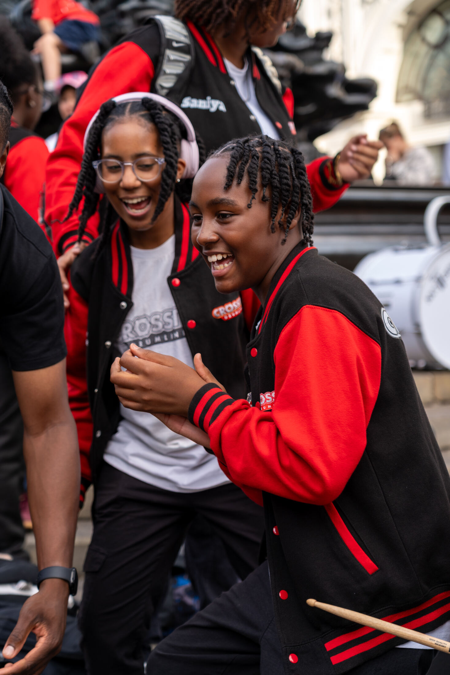 Two CrosStix drummers laughing mid-performance in red and black varsity jackets